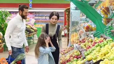 有一个小女儿的年轻父母在一家<strong>大型超市</strong>里选择新鲜的苹果。